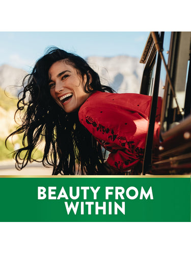 A young woman smiles while leaning out a vehicle window with mountains in the background. Text 'BEAUTY FROM WITHIN'. Biotin.