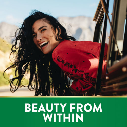 A young woman smiles while leaning out a vehicle window with mountains in the background. Text 'BEAUTY FROM WITHIN'. Biotin.