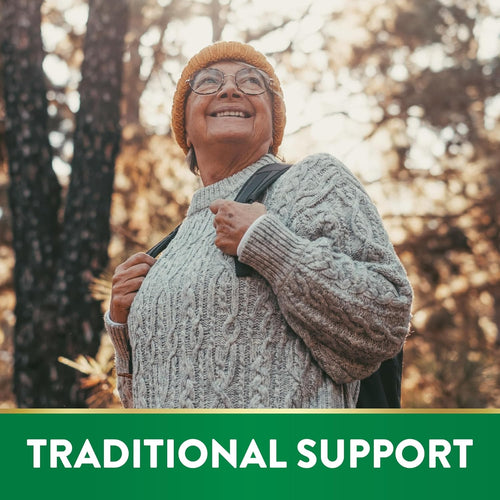 Elderly woman in a forest, wearing a hat and backpack, smiling and looking upwards. Text overlay: TRADITIONAL SUPPORT.