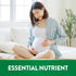 Pregnant young woman sitting on a bed, smiling and holding her belly, promoting Folic Acid benefits.