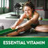 Young adult female stretching with a green resistance band on a gym floor, smiling, with the words 'ESSENTIAL VITAMIN' at the bottom.