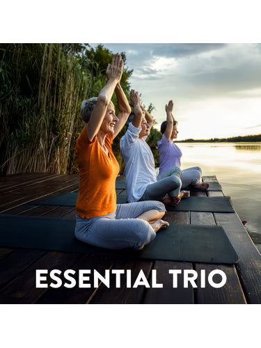 Three senior women practicing yoga with raised arms on mats by a lake at sunset. Text: ESSENTIAL TRIO.