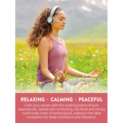 Young woman meditating in a field of yellow flowers, wearing headphones and using Calming Oil.
