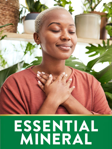 Young Black woman smiling peacefully with hands over chest, surrounded by plants. Graphic reads: ESSENTIAL MINERAL.