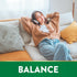 Young woman relaxing on a couch with headphones, eyes closed, smiling. The image includes the word 'BALANCE'.