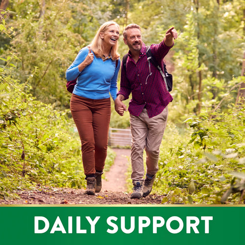 Middle-aged couple happily hiking on a forest path, holding hands while the man gestures into the distance.
