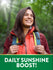 Young woman hiking in a forest, smiling towards the sun with a green graphic stating 'DAILY SUNSHINE BOOST!'
