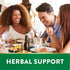 Three friends laugh and dine at a restaurant under a green 'HERBAL SUPPORT' banner.