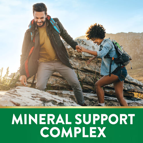 An adult man assists a woman in climbing rocks beneath a banner reading 'MINERAL SUPPORT COMPLEX'.