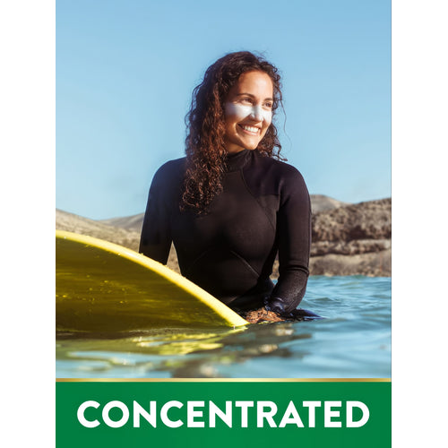Young adult woman in a wetsuit with sunscreen on her face, smiling in the water with a yellow surfboard.