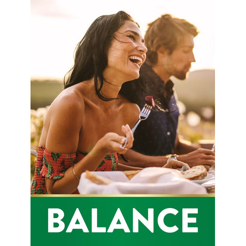 A young woman and man eating outdoors at sunset; she is laughing. Green banner below reads 'BALANCE'.