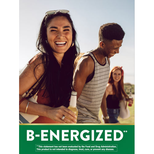 A young woman smiles, holding a 'B-ENERGIZED' bottle, while friends socialize outdoors.