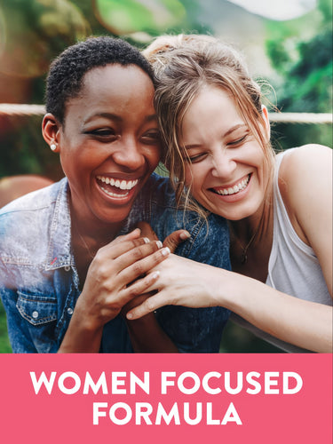 Two young women are laughing and hugging with the graphic text 'WOMEN FOCUSED FORMULA' displayed.