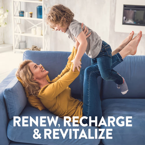 An adult woman lies on a blue couch, lifting a smiling young boy into the air as they play, with Co Q-10 nearby.